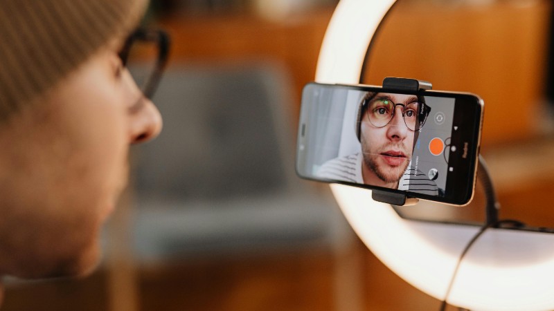 Close-up of a man recording a video with a smartphone and ring light indoors., tags: inhalte - pexel