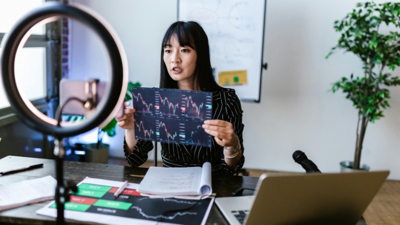 A woman vlogger discusses stock market trends using charts in a home studio., tags: die - pexel