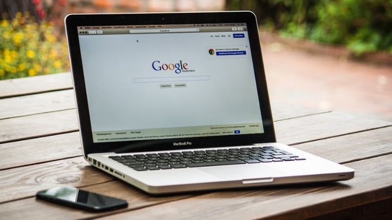 A MacBook Pro displaying Google Search on a wooden table outdoors, next to a smartphone. - A MacBook Pro displaying Google Search on a wooden table outdoors, next to a smartphone., tags: zu - pexel