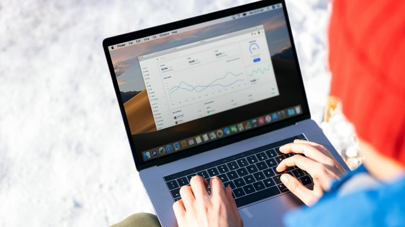 A person in a blue jacket analyzing business analytics on a laptop outdoors during winter., tags: für - pexel